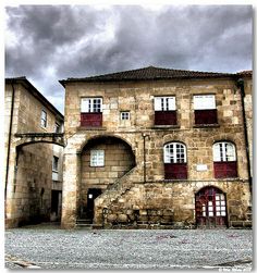 an old stone building with red shutters on the windows and stairs leading up to it