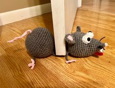 a crocheted mouse sitting on the floor next to a white pole and door