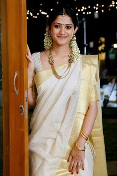 a woman in a white sari standing next to a wooden door with lights on it