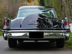 an old black car is parked on the side of the road in front of some trees