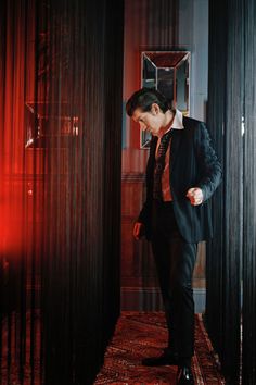 a man in a suit and tie standing next to tall black pillars with red curtains