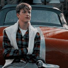 a young man sitting on the hood of a red car