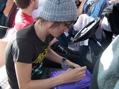 a young man sitting on the ground looking at his cell phone while wearing a beanie