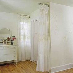 a bedroom with white walls and wood flooring has a mirror, dresser, and bed