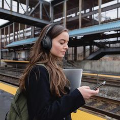 a woman with headphones is looking at her cell phone while waiting for the train