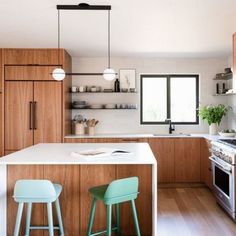 two stools sit at the kitchen island in this modern style kitchen with wood cabinets and white countertops