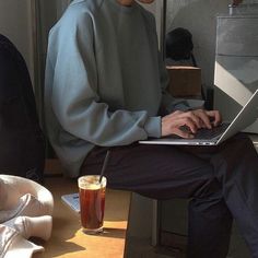 a man sitting in front of a laptop computer on top of a wooden table next to a cup