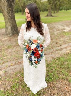 a woman in a white dress holding a bouquet of red, orange and blue flowers