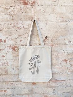 a tote bag hanging on a brick wall with flowers drawn on the front and side