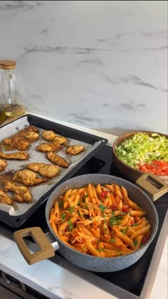 two pans filled with pasta and chicken on top of a kitchen counter next to other food