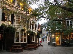 an empty city street with tables and benches in front of buildings on either side of the street