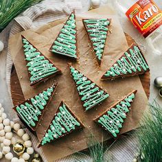 cookies decorated with green icing on top of a wooden cutting board next to christmas decorations