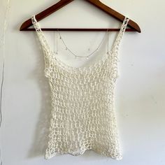 a white crocheted tank top hanging on a wooden hanger