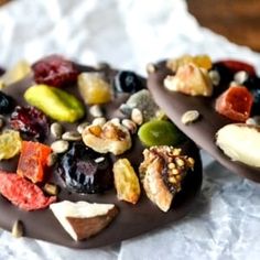 two pieces of chocolate with nuts and dried fruit on top sitting on a piece of wax paper