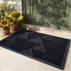 a black door mat sitting on the side of a house with sunflowers next to it