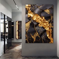 an abstract painting in gold and black on a gray wall next to a wooden floor