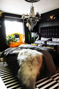 a bedroom with black walls and white fur on the bed, chandelier hanging from the ceiling