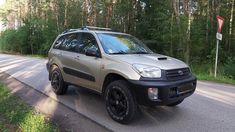 a silver suv parked on the side of a road in front of some trees and bushes