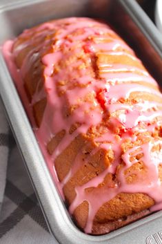 a loaf of cake with pink icing sitting in a pan on top of a table