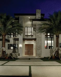 a large white house with palm trees in the front yard and lights on at night