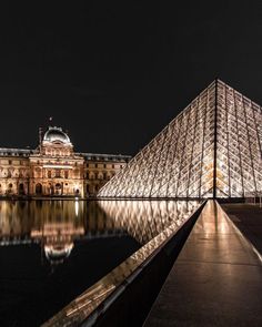 the pyramid is lit up at night in front of a building with its reflection on the water