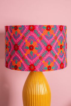 a yellow vase with a pink and blue lamp shade on it's side against a pink wall