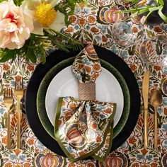 a place setting with napkins and flowers on the table top, along with gold utensils