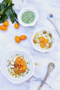 two white bowls filled with food next to oranges and other fruits on a table