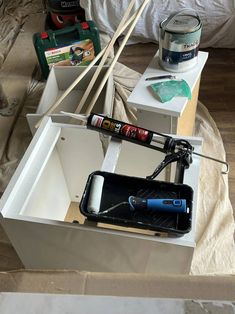 an open box with paint and tools in it on top of a wooden floor next to a bed