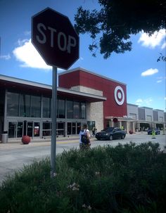 a stop sign in front of a target store with people walking by it and cars parked on the street