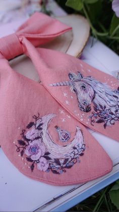 two pink bow ties with unicorns on them are laying next to some purple flowers