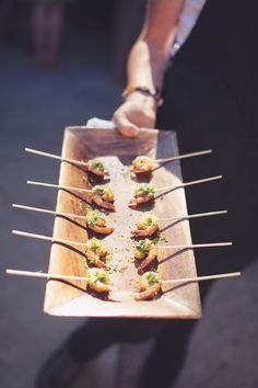 a person holding a wooden tray with food on it and toothpicks in the middle