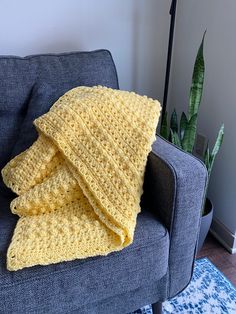 a yellow crocheted blanket sitting on top of a blue couch next to a potted plant