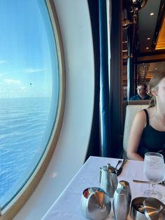 a woman sitting at a table in front of a large window with the ocean outside