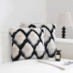 two black and white pillows sitting on top of a couch next to a lamp with a book