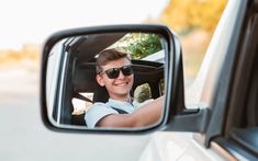 a young man wearing sunglasses is smiling in the side view mirror of a white car