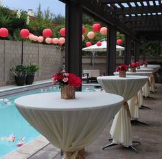 tables with white tablecloths and red paper lanterns hanging from the ceiling next to a swimming pool