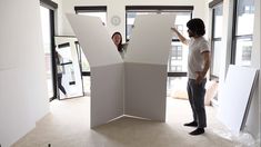 a man and woman standing in an open room with large white panels on the wall