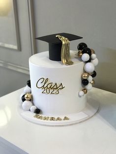 a white cake with black and gold decorations on it's side, topped with a graduation cap