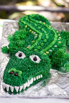 there is a cake made to look like a green alligator's head on tin foil