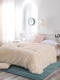 a bedroom with white walls and wood flooring has a large bed covered in fluffy blankets