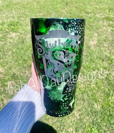 a person holding up a green and black tumbler cup in their hand on the grass