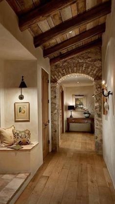 a long hallway with stone walls and wooden flooring is lit by two lights on either side