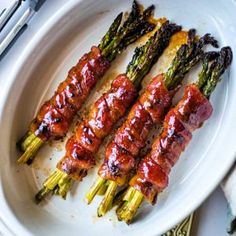 asparagus wrapped in bacon on a white plate with silverware and utensils