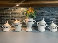 four white vases with flowers in them sitting on a counter