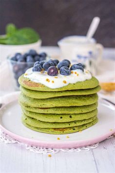 a stack of green pancakes topped with blueberries and whipped cream