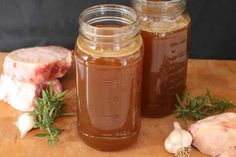 two jars filled with liquid sitting on top of a wooden table next to garlic and meat