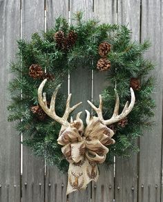 a wreath with antlers and pine cones hanging on a wooden wall next to a fence