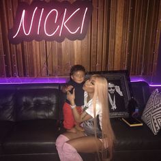 a woman sitting on top of a black couch next to a little boy in front of a neon sign