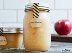 two jars filled with apple jam sitting on top of a table next to an apple